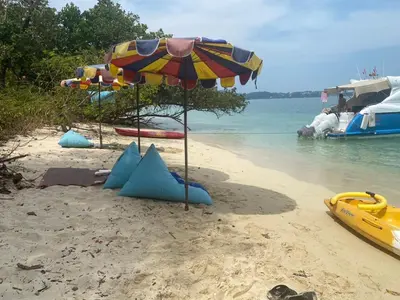a beach with an umbrella and some boats in the water at Private Beach Camping on island at Koh Lon Island in Ko Lon