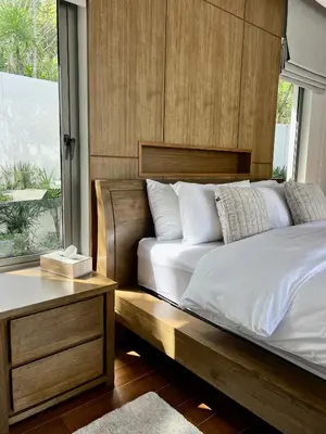 a bed with a wooden headboard next to a window at Bang Tao Anchan Flora 3 bd in Ban Phru Champa
