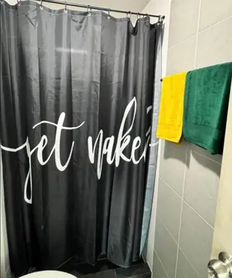 a bathroom with a black shower curtain with a let wake sign at Lux Center Apartment in Kathu