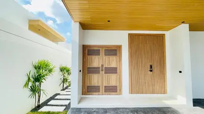 a wooden door in a white house with trees at Mouana Residence Song Khun Chalong 8910 in Phuket Town