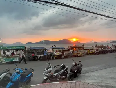 a group of scooters parked on a street with the sunset at Sea View & Pool Apartment in Phuket Town