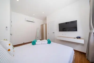 a white bedroom with a large white bed and a flat screen tv at Goldena Twin Project - 3 Bedrooms Pool Villa in Kamala Beach