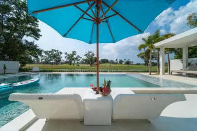a table with an umbrella next to a swimming pool at Lumière Villas Phuket - Golfside Retreat in Laguna in Laguna Phuket