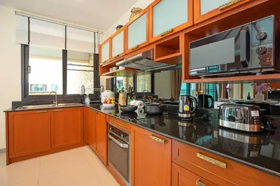 a kitchen with wooden cabinets and black counter tops at Tropical 2BR Pool Villa 3D12 in Gated Residence Rawai VIP Villas in Rawai Beach