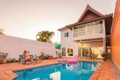 a house with a pool and a woman sitting in a chair next to a house at Family Holiday 3BR Pool Villa Lancelot 2 in Rawai Beach