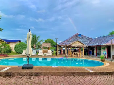 a pool with a umbrella and chairs and a restaurant at Water's Edge Resort , in Panwa Beach