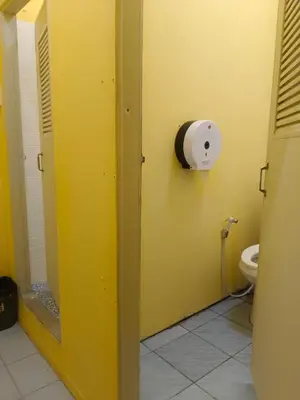 a bathroom with a toilet paper dispenser on a yellow wall at 3Plus1 Hostel Patong in Patong Beach
