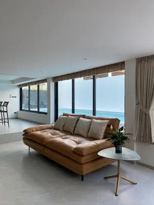 a brown leather couch in a living room with windows at Mountain breeze villa phuket in Ban Bang Khu