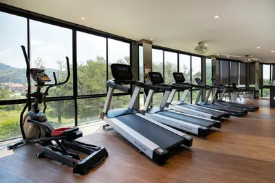 a row of cardio machines in a gym with windows at Tropics Kamala 2BR Apartment CTG L602-3, Several Pools, Gym & Rooftop in Kamala Beach