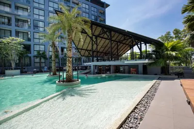 a swimming pool with palm trees in front of a building at Enjoy Tropical Bliss in Kamala Suite CTG L704, Top Facilities, near FantaSea & Café Del Mar Beach Club in Kamala Beach