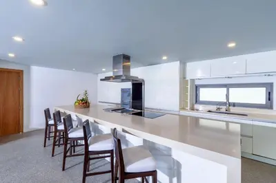 a kitchen with white cabinets and a bar with chairs at Villa Amankara in Phuket Town