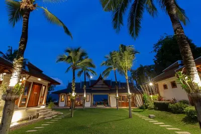 a house with palm trees in front of it at Villa Talaefun - Luxury Oceanfront Fully Serviced in Kamala Beach