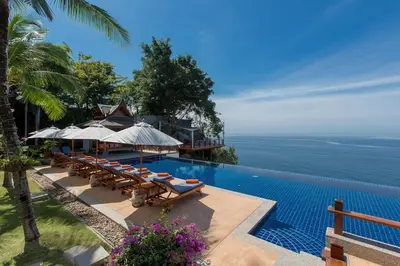a pool with chairs and umbrellas next to the ocean at Villa Talaefun - Luxury Oceanfront Fully Serviced in Kamala Beach