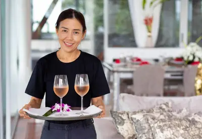 a woman holding a tray with two glasses of wine at Villa Laemsingh 2 Oceanfront Fully Serviced in Surin Beach