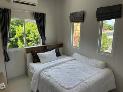 a bedroom with a bed with white sheets and two windows at Family House in Bang Tao in Ban Thalat Choeng Thale