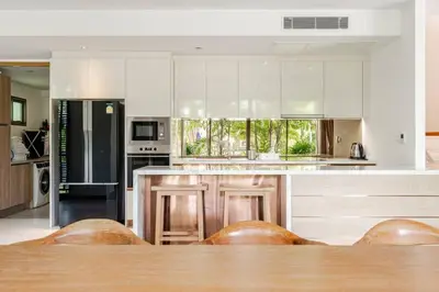 a kitchen with white cabinets and a wooden table at WEG Laguna Residence in Thalang