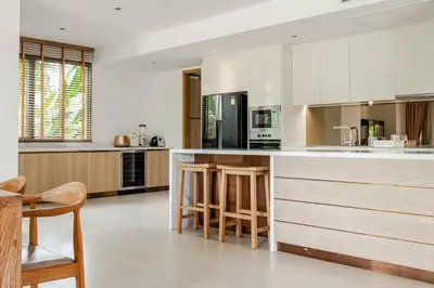 a kitchen with white cabinets and a bar with stools at WEG Laguna Residence in Thalang