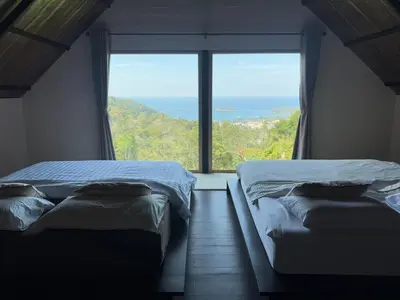 two beds in a room with a large window at Choncharm house 2 in Kata Beach