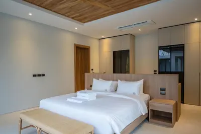 a bedroom with a large white bed with a wooden headboard at Mouana Breeze Mai Khao 4-bedroom Pool Villa 9918 in Mai Khao Beach