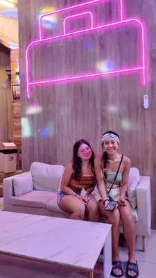 two women sitting on a couch under a neon sign at Hangover #1 Hostel Patong in Patong Beach
