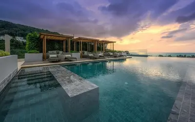a swimming pool with chairs and the ocean at sunset at Seaview, cozy apartment, Surin in Surin Beach