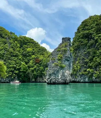 a boat in a body of water with a rock formation at Villa Miyoko Ko Yao Noi Enjoy nature's beauty and stunning sunsets in Ko Yao Noi
