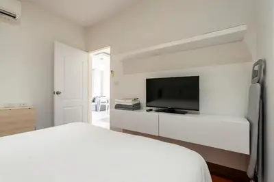 a white bedroom with a bed and a flat screen tv at The Lago by Villacarte in Rawai Beach