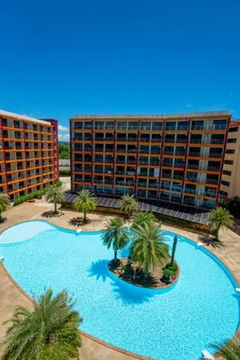 a large swimming pool with palm trees in front of a building at The Urban Tropical Apartments in Mai Khao Beach