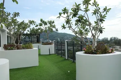 a balcony with white walls and trees and grass at Apartment by the sea Kamala Beach A502 in Kamala Beach