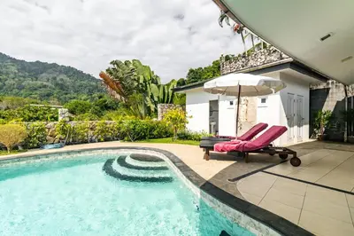 a pool with two chairs and an umbrella next to a house at Luxurious & Quiet Pool Villa Orchid in Nai Yang Beach