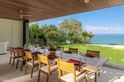 a dining room with a table and chairs and the ocean at Villa Amarasara in Phuket Town