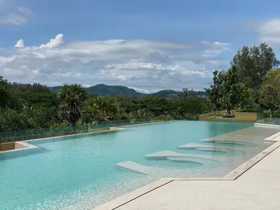 a swimming pool with blue water and mountains in the background at 1 bdr Mountain View Apartment 50 m from Bangtao Beach in Bang Tao Beach
