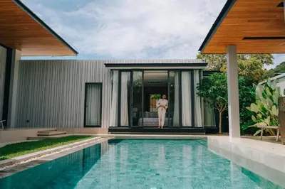 a woman standing outside of a house with a swimming pool at Botanica Foresta Villa in Thalang
