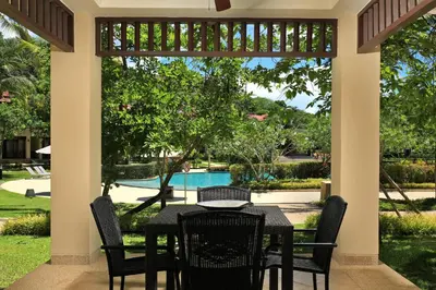 a dining table and chairs on a porch with a view of a pool at Tropical Holiday Home at Laguna Phuket in Layan Beach