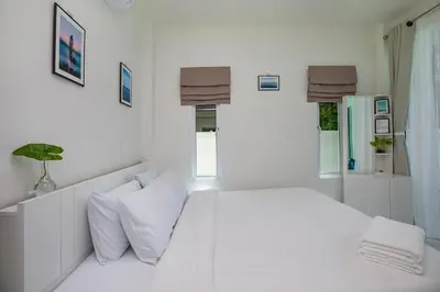 a white bedroom with a bed and two windows at The White House Kamala Beachfront in Kamala Beach