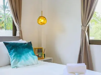 a bedroom with a bed with a blue pillow and a window at Wink Garden 3 Bedrooms Bangtao Beach Phuket in Ban Thalat Choeng Thale