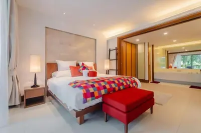 a bedroom with a large bed and a red stool at Elegant Beachfront 3BR Condo at Pearl of Naithon in Nai Thon Beach