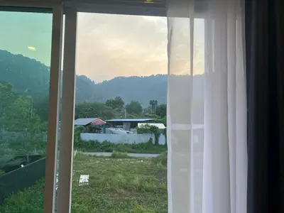 a window with a view of a field and a house at Anda Mantham Hill in Ban Bang Rong