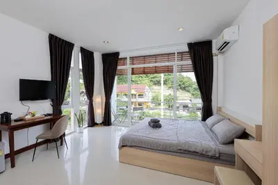 a bedroom with a bed and a desk and a window at StayKa Suites in Karon Beach