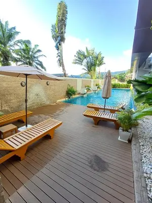 a deck with benches and an umbrella and a swimming pool at Chic Condominium in Karon Beach