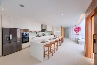 a kitchen with white cabinets and a long island with bar stools at Designer 3BR Pool Villa in New Build LuxPride 4 L8 Residence in Bang Tao Beach