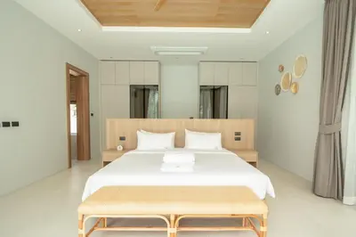 a bedroom with a large white bed with a wooden headboard at Mouana Breeze Mai Khao 4-bedroom Pool Villa 9922 in Mai Khao Beach