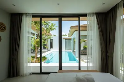 a bedroom with a view of a swimming pool through windows at Mouana Breeze Mai Khao 4-bedroom Pool Villa 9920 in Mai Khao Beach