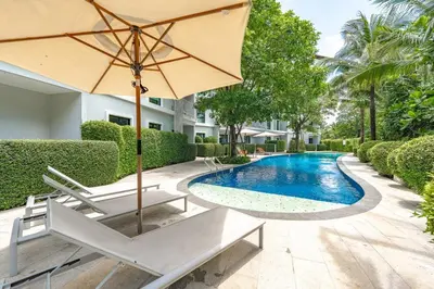 an umbrella and chairs next to a swimming pool at C188 Modern Condo Pool Gym & Walk to Rawai Beach in Rawai Beach