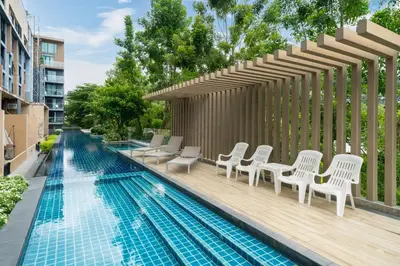 a swimming pool with white chairs and a wooden deck at 1 Bedroom Apartment - The Aristo Resort by HCR in Surin Beach