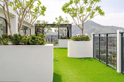 a white fence with green grass and trees at Cozy New 1-Bedroom Apartment with Pool, 5 Min Walk to Kamala Beach in Kamala Beach