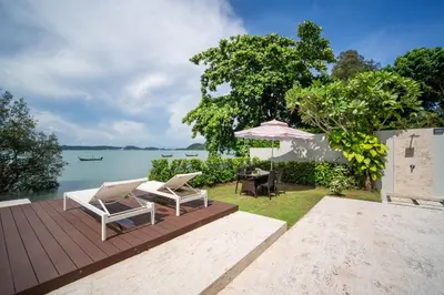 a patio with chairs and an umbrella next to the water at \u62c9\u5a01Eva4 \u4e09\u5367\u5ba4\u4e00\u7ebf\u6d77\u666f\u522b\u5885 \u8fd1\u62c9\u5a01\u6d77\u9c9c\u5e02\u573a \u8d85\u5e02 24\u5c0f\u65f6\u5c0f\u533a\u5b89\u4fdd in Ban Saiyuan (1)