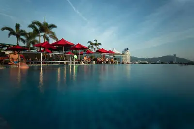 a swimming pool with red umbrellas and people sitting at Beachfront 1 BR Hotel Infinity Pool Patong Phuket in Patong Beach