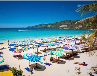 a group of people on a beach with umbrellas at The Kris Luxury in Patong Beach