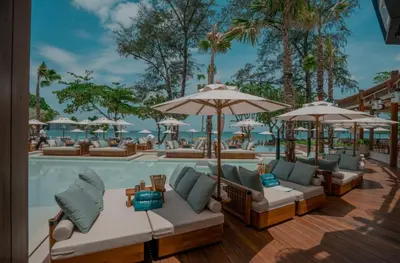 a pool with chairs and umbrellas next to a resort at The Kris Luxury in Patong Beach